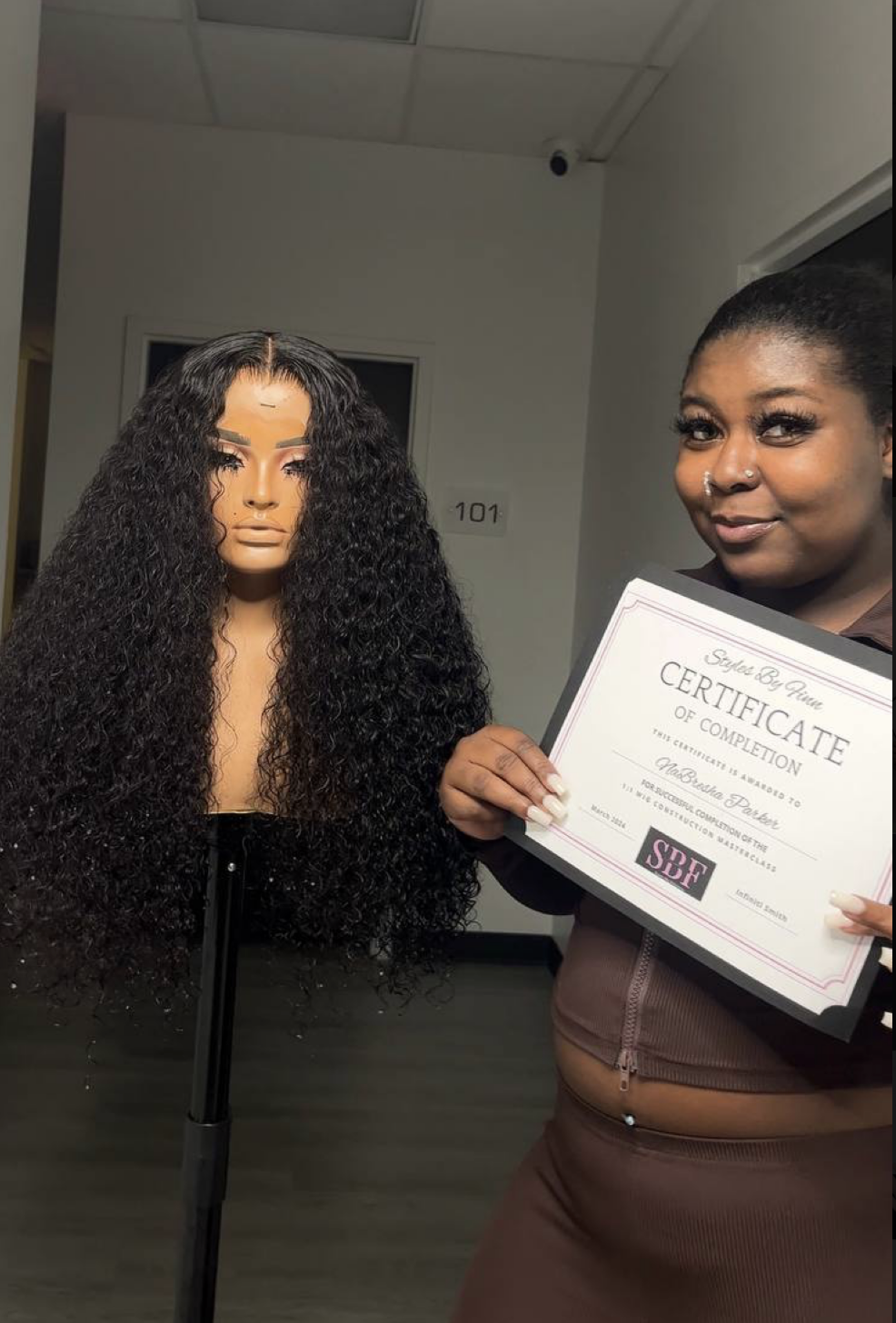Graduate holding SBF certificate next to long curly wig